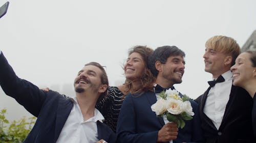 A Couple Kissing while a Man Taking a Group Picture