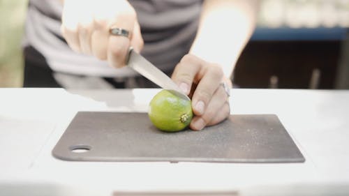 Person Slicing A Lime Fruit On A Cutting Board