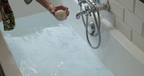 A Person Dropping a Bath Bomb in a Bathtub