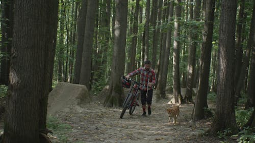 A Man Walking with His Dog while Carrying His Bike