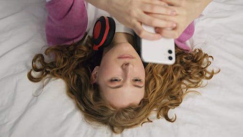 Woman Lying on Bed Using Cellphone