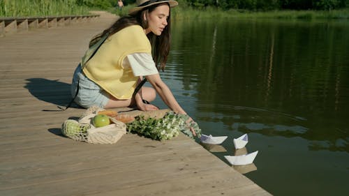 A Woman Placing Paper Boats on a Lake 