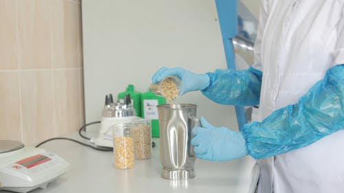 A Scientist Pouring Raw Rice on a Stainless Beaker