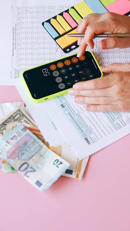 A Person Using Calculator while Writing on Sticky Notes