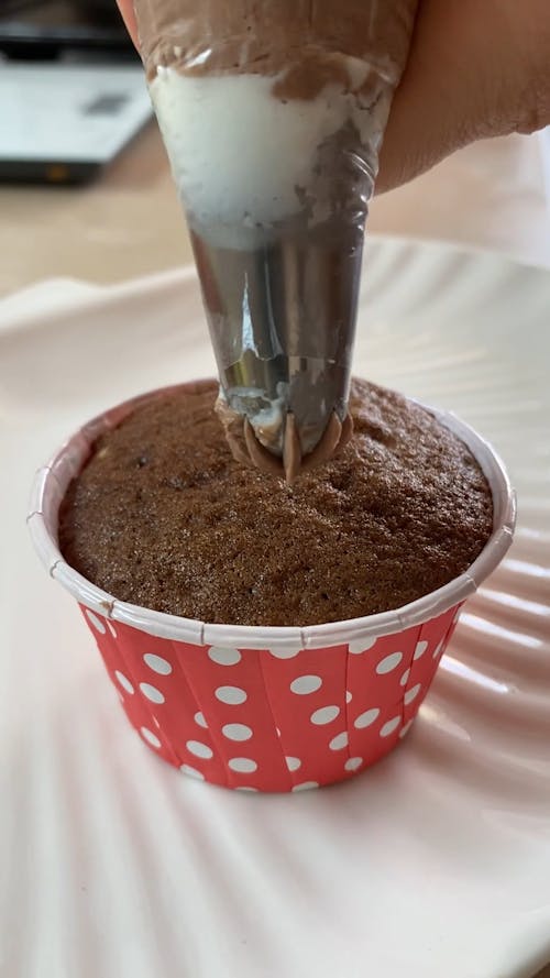 A Person Putting Icing on a Cupcake