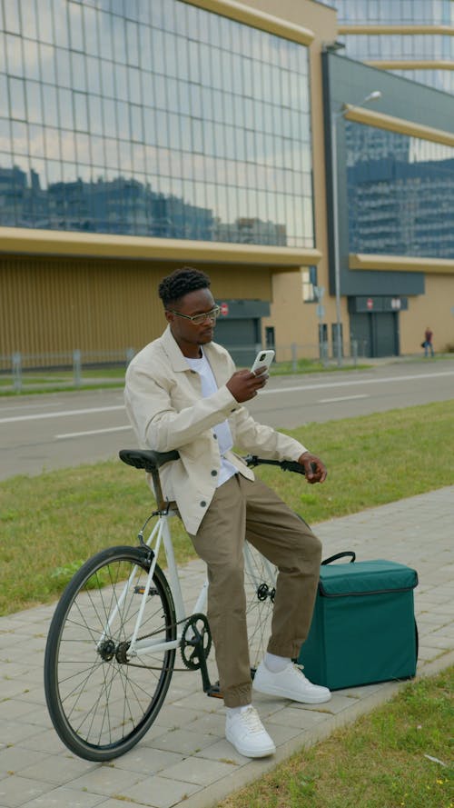 A Man Sitting on His Bike and Looking at His Smartphone 