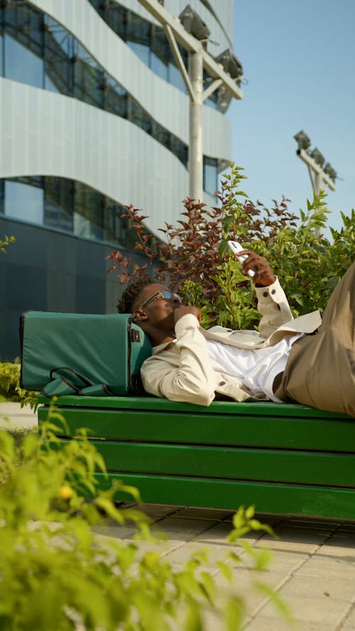 Man Lying on Bench While Using Cellphone