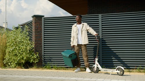 A Man Carrying a Thermal Bag Standing Beside a Scooter