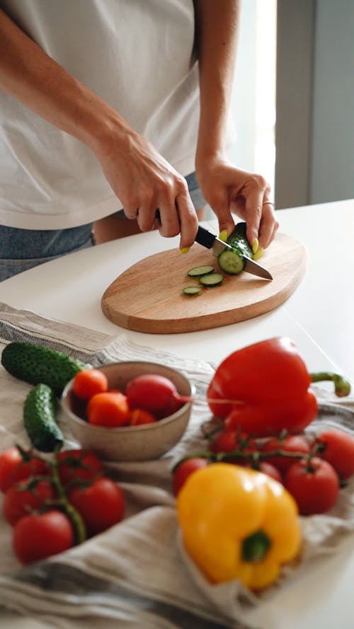 Person Slicing Cucumber on a Wooden Chopping Board