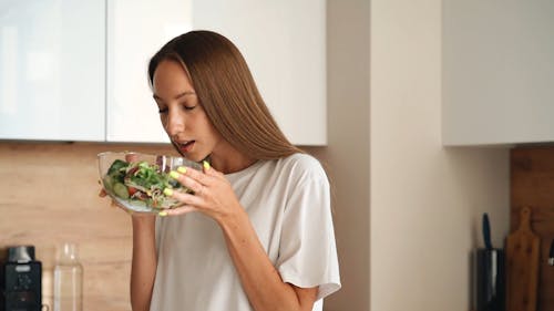 A Woman Holding and Smelling a Bowl of Salad 
