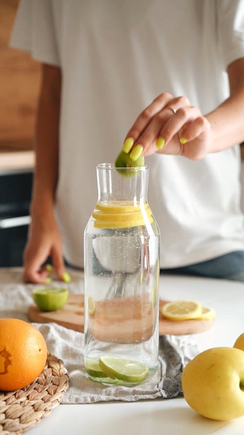 A Person Putting a Slice of Lemon and Lime on a Glass Bottle