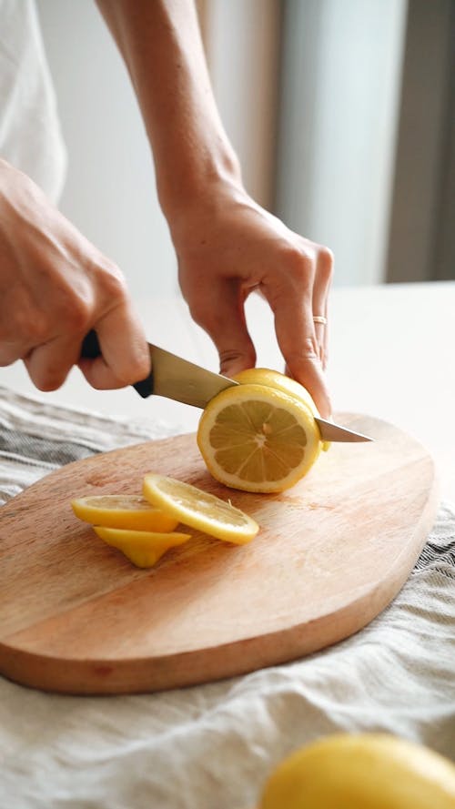 A Person Slicing Lemon on Wooden Chopping Board