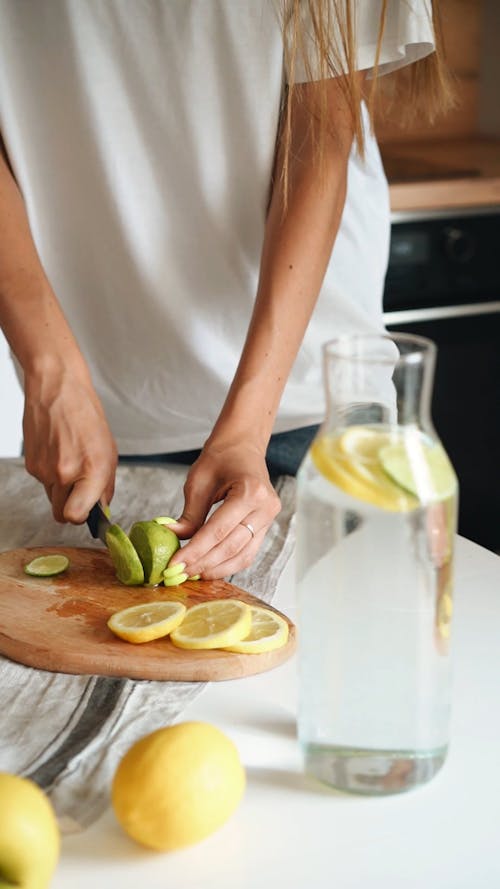 A Person Slicing a Lime while Putting on a Glass Bottle with Water