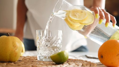 A Person Pouring Water with Lemon on a Drinking Glass