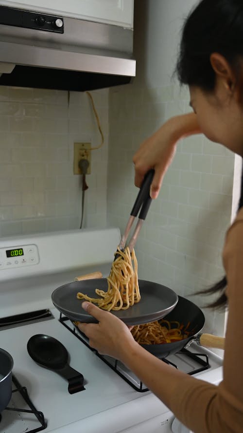 A Woman Getting Pasta from a Pan on a Stove