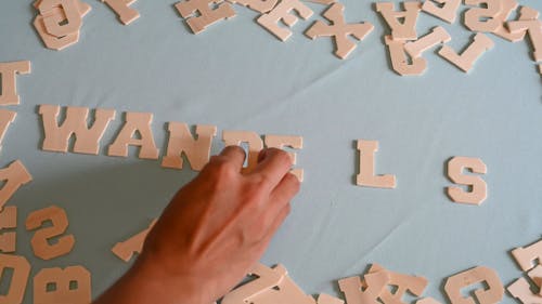 A Person Spelling Wanderlust Using Wooden Letters