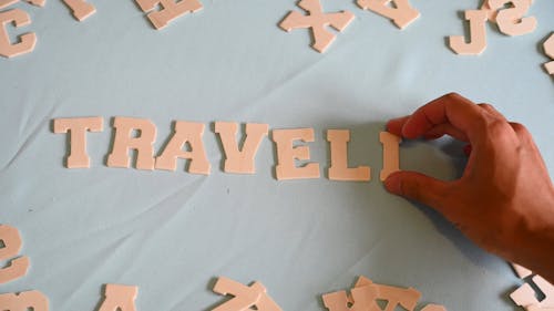 A Person Spelling Travelling Using a Wooden Letters