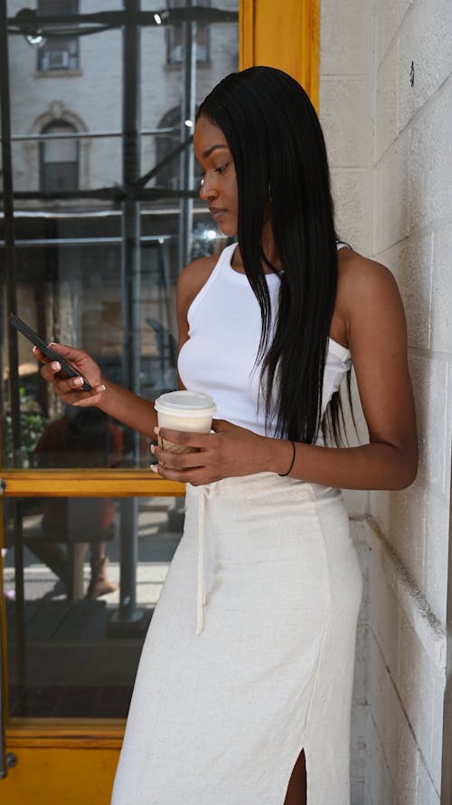 A Woman Using a Cellphone while Holding a Drink