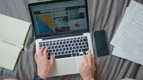 A Person Using Laptop while Writing on Notebook