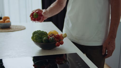 A Person Putting the Bowl of Vegetables and Fruits on a Kitchen Countertop