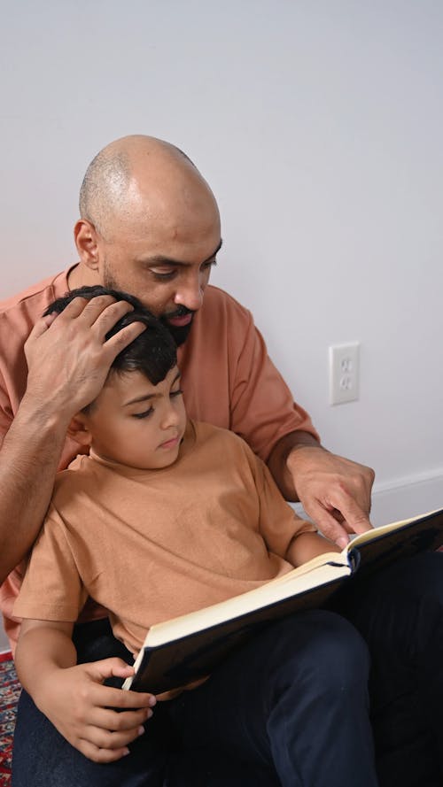 Boy Leaning on a Man While Reading a Book