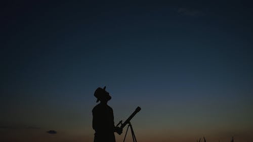Silhouette of a Man Standing by his Telescope  