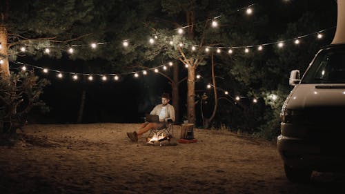 A Man Sitting by a Campfire Using a Laptop 