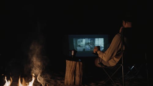 A Man Sitting by a Campfire and Watching a Movie 