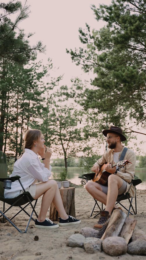 A Woman Listening to a Man Singing and Playing Guitar Outdoors