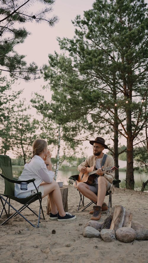 A Man Playing Guitar for a Woman at a Campsite 