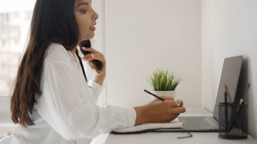 Woman Writing on Notebook while using Laptop