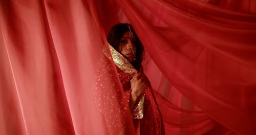A Woman Wearing Traditional Clothing Standing Behind Red Sheer Fabric