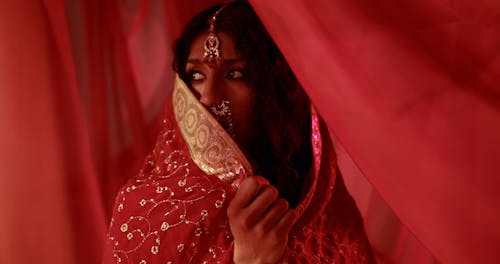 A Woman Under Red Sheer Fabric Seriously Looking at Camera