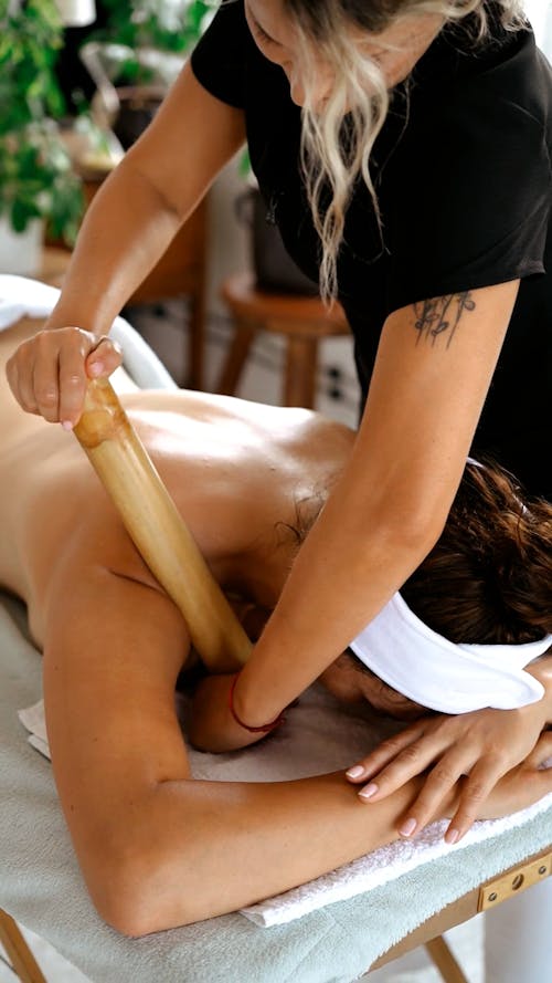 A Therapist Using a Rolling Pin in Massaging a Client's Shoulder