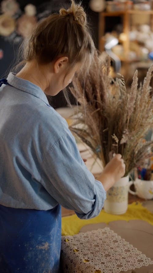 A Woman Holding a Dried Flowers while Putting on the Table