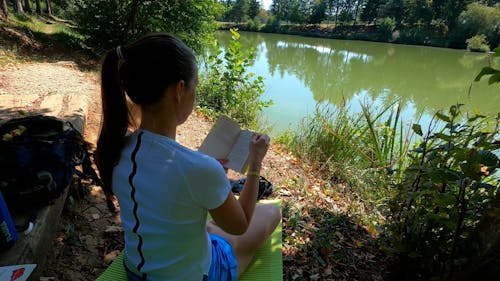 A Woman Reading a Book while Sitting Near the Lake