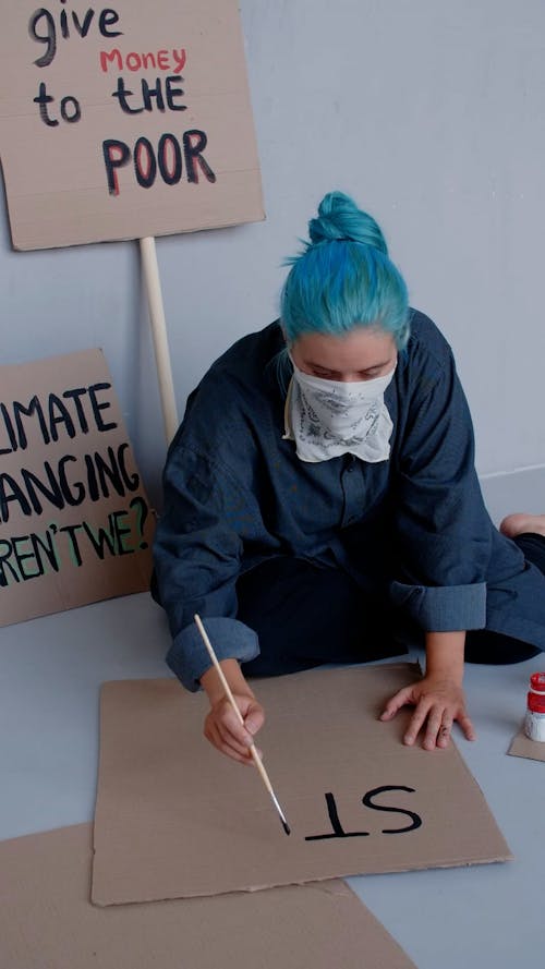 A Woman with Blue Hair Writing on a Cardboard