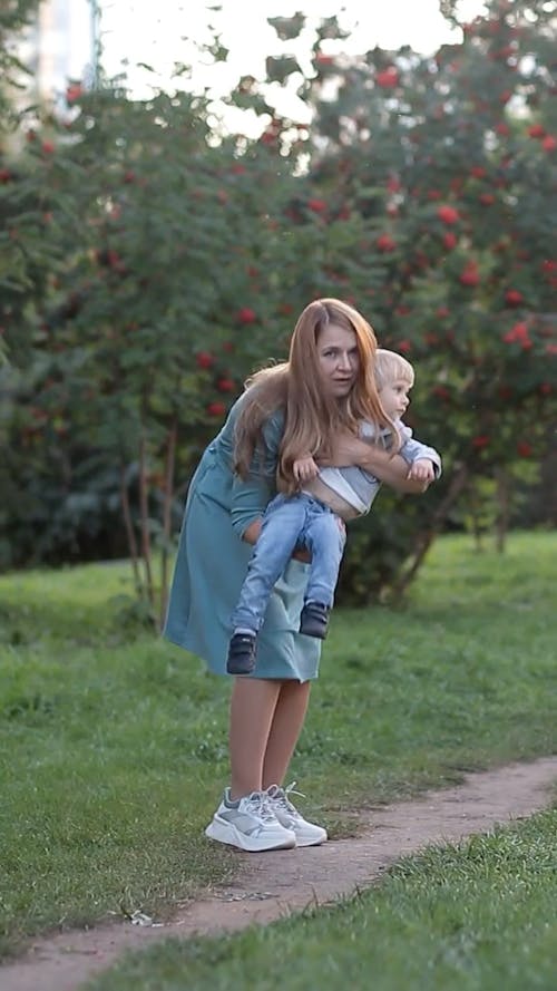 A Woman Walking and Carrying her Son in her Arms