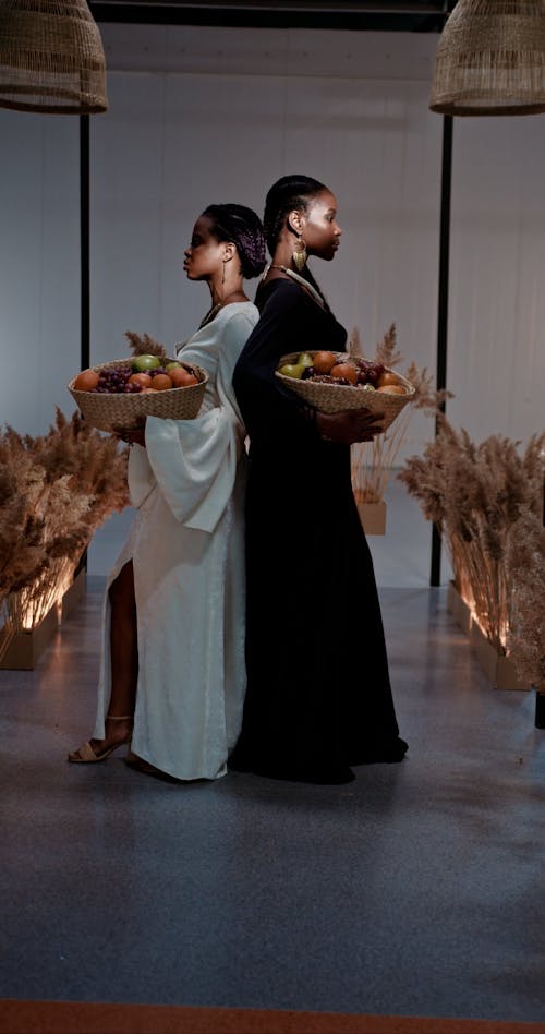 Woman Standing Back to Back while Holding a Basket of Fruits