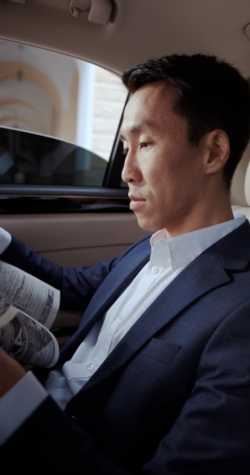 A Man Reading a Newspaper while Sitting at the Back Seat of a Car