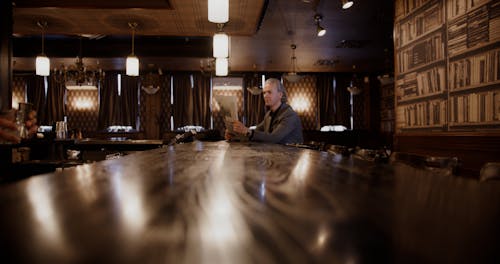 An Elderly Man Reading a Newspaper while Drinking on a Bar Counter