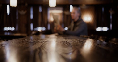 An Elderly Man Reading a Newspaper while Drinking on a Bar Counter