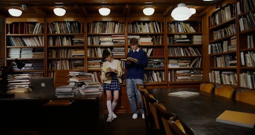 A Man and Woman Leaning on a Bookshelf while Reading a Book