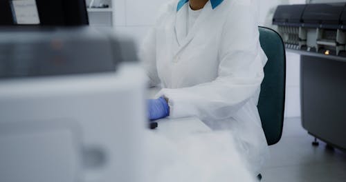 A Woman Wearing Laboratory Gown and Face Mask Working in Front of a Computer