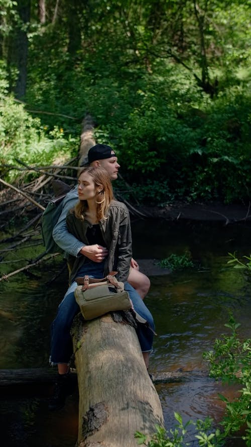 A Couple Sitting on a Tree Trunk over a Stream