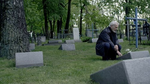 Elderly Man Crouching in Front of a Tombstone