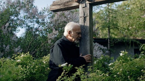A Grieving Elderly Man Embracing a Wooden Cross