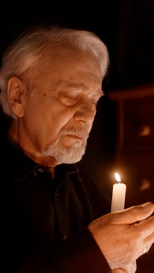 An Elderly Man Looking at the Lighted Candle He is Holding