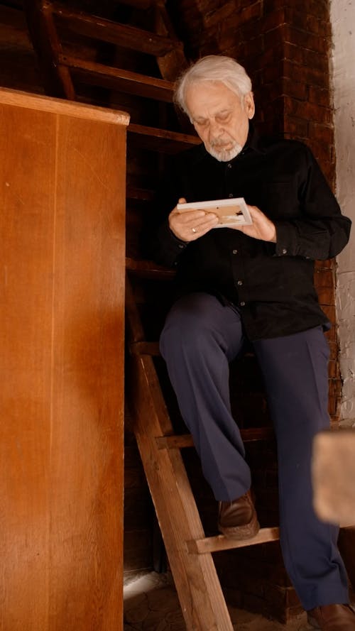 A Sad Elderly Man Looking at the Picture Frame He is Holding