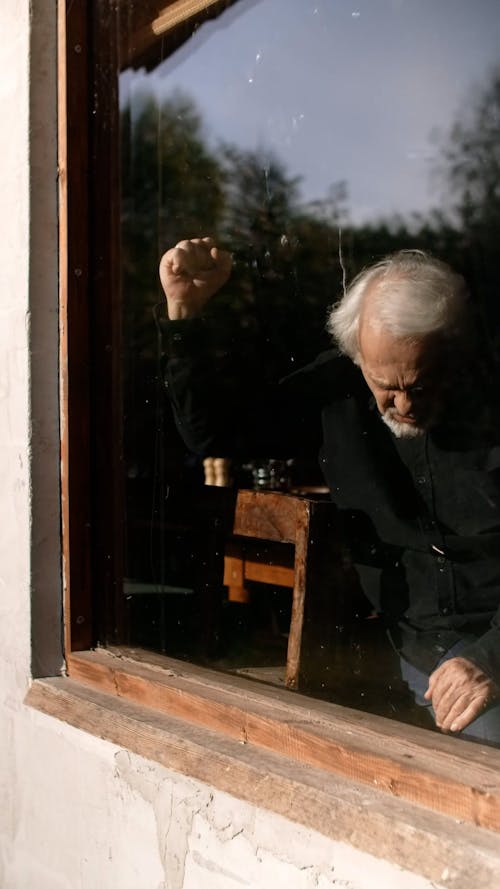 A Sad Elderly Man Hitting the Window Glass
